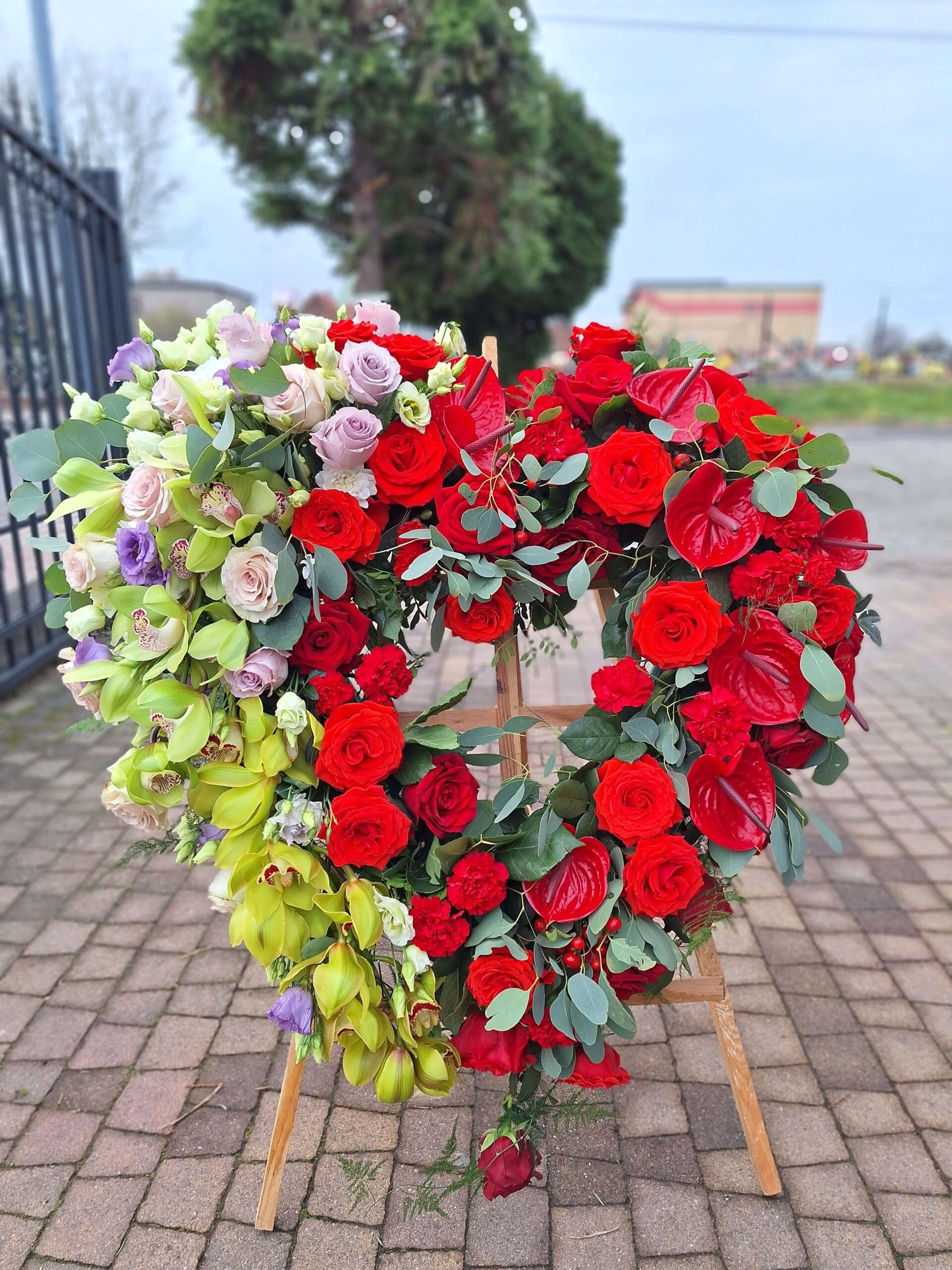 Wieniec pogrzebowy w kształcie serca z czerwonych i zielonych kwiatów elegancka kompozycja