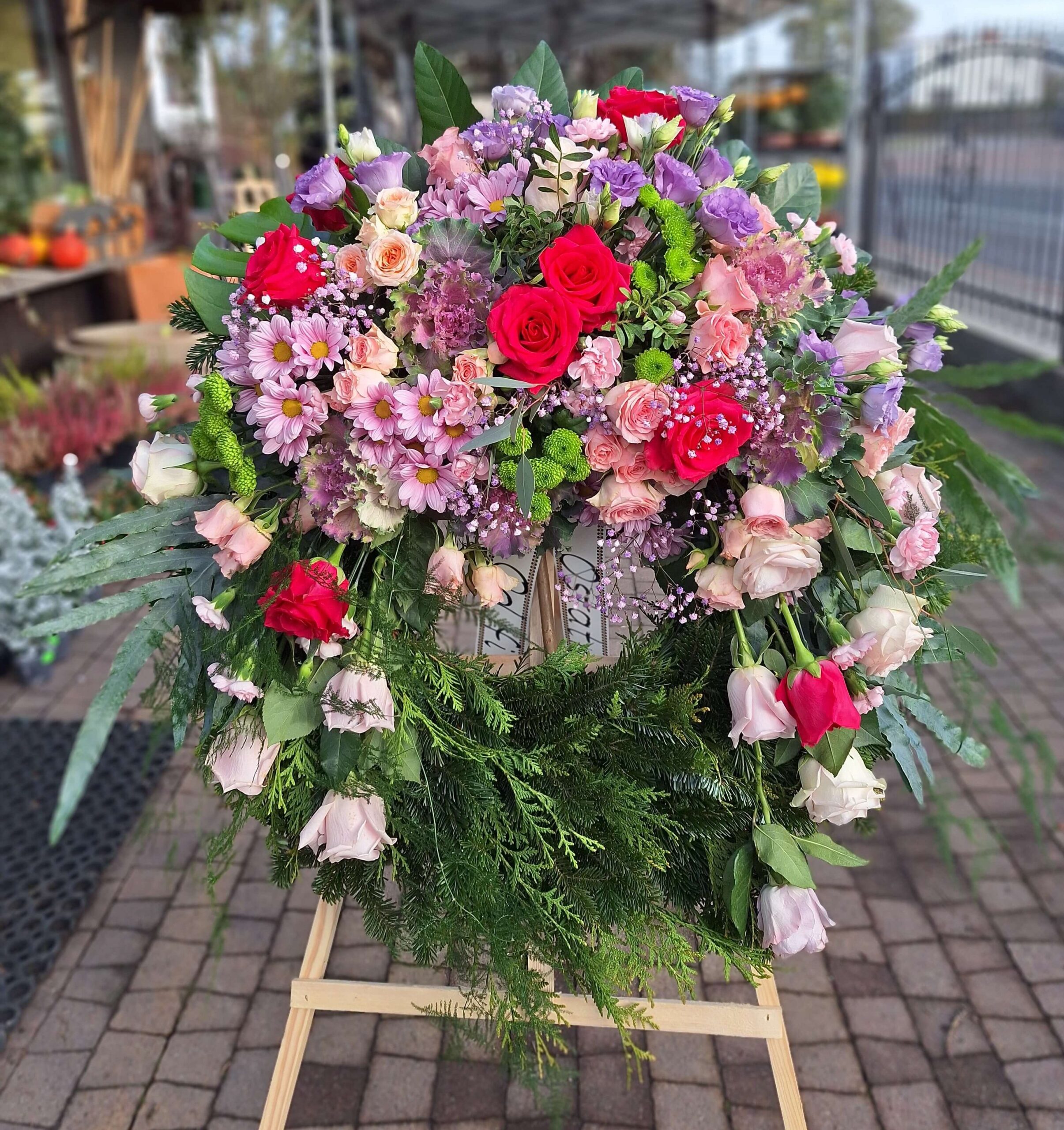 Wieniec pogrzebowy z różami, eustomami i margerytkami w pastelowych odcieniach, ozdobiony zielenią
